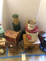 Photo showing assorted vintage and antique tins, including decorated rectangular and cylindrical tins, creamery biscuit tins, tea tins, and a small floral ceramic coin bank.