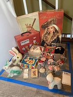 Wide view of lot showing vintage toys including paper mache bunnies, plaster lamb, Barbie in box, Peanuts lunch box, miniature chairs, and other assorted vintage toys.