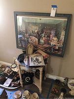 Full scene showing large framed kitchen wall art above small wooden table cluttered with vintage items including rotary phone, records, cups and papers.