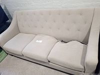 Full view of the cream fabric 3-seat sofa couch showing the seat cushions with visible damage on two cushions.
