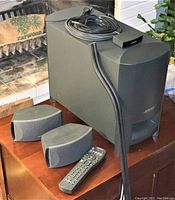 Full view of BOSE subwoofer, two satellite speakers, remote control, wiring cords coiled on top of subwoofer, and speaker stands