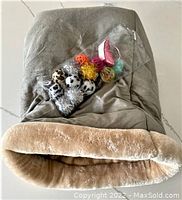 Gray Armarkat cat sack bed with plush beige interior and sealed package of assorted new cat toys on top.