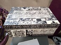 Top and side view of black and ivory storage box with decorative patterns and phrase Live Laugh Love.