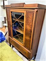 Front view showing wood frame, glass front with lattice design, and bottom drawer with metal pulls.