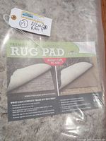 Clear packaging showing the label 'Premium Dual Surface Rug Pad' and product benefits, indicating dual surface for hardwood and carpet use.