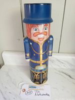 Full view of the nutcracker tin showing the blue uniform, orange mustache, and removable blue hat.