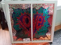 Full view of the handmade stained glass window showing the word LOVE split across two panels with colorful and intricate patterns.