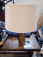 Full view of table lamp showing white fabric drum shade and copper-colored metal base on wooden table.