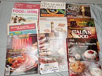Top-down photo showing all 12 vintage cooking magazines and cookbooks arranged in a grid, titles visible including Food & Wine, Great Chefs, Ideals Christmas Cookbook, Italian cookbook, Mohawk Encyclopedia of Alcoholic Beverages.