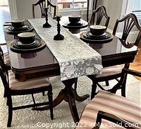 Full view of the mahogany wood dining table set with glass top and chairs around it, table runner and plates displayed to show condition and style.