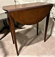 Side view of the wooden drop leaf side table folded down, showing shape and leg condition.