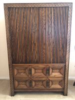 Front view of closed wooden armoire with carved details and drawers.
