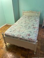 Single-sized bed frame with floral decor and matching floral mattress in a room with teal walls and parquet floor