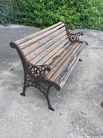 Side angled view showing curved cast iron armrest and legs with weathered wooden seat and back slats, highlighting peeling paint and wood damage.