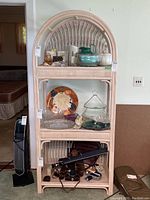 Front view of light pink bentwood shelf with three shelves containing various items.