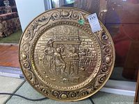 Full view of the round brass plaque with intricate historical scene and ornate border.