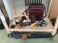 Photo of the lot showing Cruisaire camera bag, Minolta SR-1 camera in brown leather case, lens in brown leather case, round filter in tan case, All-Mite flash unit, black tripod with patterned strap, and other camera accessories on a wicker shelf.