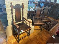 Four antique wooden dining chairs including one armchair and three side chairs with carved shield motifs on the backrest and turned spindle supports.