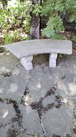 Full view of curved concrete bench seat and two pedestal supports positioned on stone surface in garden backyard.