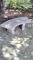 Curved concrete bench fully assembled in outdoor patio setting on stone flooring.