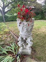 Full view of concrete planter and base in garden setting, planter contains red flowering plant.