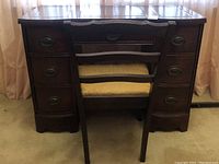 Front facing photo of vintage wood desk with multiple drawers and matching chair pushed under the center drawer.