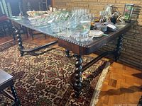 Side view of dark wood dining table with intricate barley twist legs and glass top, showing carved edges and overall condition of surface.