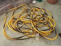 Tangled heavy duty extension cord yellow and black insulated, male and female plug ends visible.