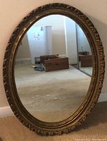 Full view of the oval framed mirror showing its size and shape against a wall and floor background.