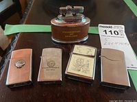 Front view of all five lighters arranged in a row on a wood surface. Visible branding includes Prudential of England, Shell medallion, United Wireless Penfield, and ship image.