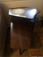 Two-tier wooden side table from top view showing triangular shaped tiers with cylindrical metal support posts and some surface wear.
