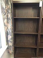 Front view of dark brown wooden shelving unit with multiple shelves, showing adjustable shelf positions.