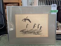 Signed goose-themed print by Albert J. Casson in silver frame with gray matting, showing five Canada geese, one flying and four standing.