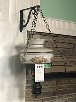 Side view of the swag lamp hanging from the metal bracket against a white wall with stone background showing floral glass shade and chains.