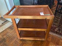 Wooden tea trolley showing the side view with upper tray and two lower shelves, wheels visible.