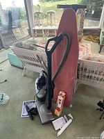 Full view of TriStar vacuum cleaner with hose, attachments, ironing board, fire extinguisher box, and door closer parts on carpeted floor