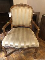 Front view of vintage wood framed armchair showing carved details and beige striped upholstery.