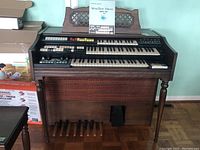 Full view of the wooden console organ with two keyboards, pedalboard, and manual placed above the keyboards.