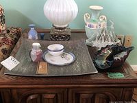 Photo of entire lot on wooden table, showing the Wedgwood bud vase, ceramic jug with nautical motif, art glass bowl, stack of Japanese porcelain teacup and plate, decorative Canfloyd plate, and glass sailboat figurine.
