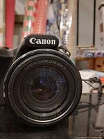 Front close-up of Canon camera lens marked 'CANON ZOOM LENS 50X IS' and focal length specs.