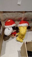 Photo showing both Snoopy and Woodstock lighted Christmas figures on the floor with cords visible and background wall.