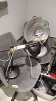 Greenmade portable heater and metal desk lamp on gray chair, showing the heater's reflective metal back and the lamp's adjustable arm and shade.