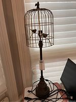 Full view of birdcage style metal table lamp with bird figurines inside cage and on top, showing overall condition and lamp structure.