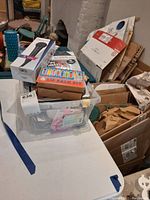 Photo showing various boxed items, including a microphone box and colorful packaged kits inside a clear plastic container on a white table.