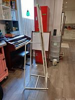 Full view of the stand mirror in a room setting, showing the white metal frame and base stand with rectangular mirror surface.
