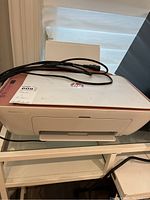 Top and front view of HP DeskJet 2742e printer showing overall unit and power cord coiled on top.