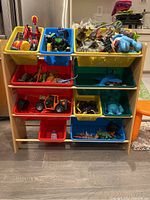 Front view of wood shelving unit loaded with colorful plastic bins containing toys (not included).