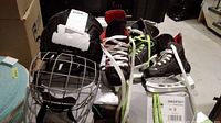 Photo showing two pairs of ice hockey skates, one Bauer youth size 7 and the other with unknown size, along with a black Lil Sport hockey helmet with cage.