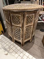 Front angle view of the hexagonal wooden table base showing carved geometric cutouts and distressed finish.