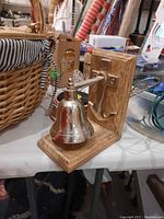 Wooden wall mounted silver bell with lever, shown on table beside a woven basket and other items